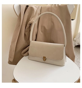 Detailed close-up of cream baguette bag with vintage brass buckle on a white stool
