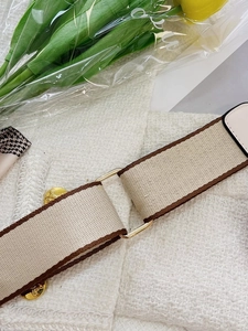 Detail of wide woven canvas strap in beige and brown with golden metal rings