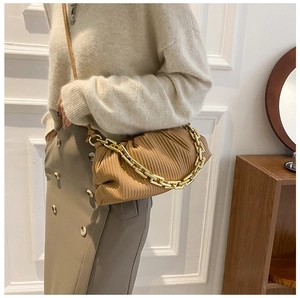 Detail of a ginger pleated cloud bag with chunky gold chain strap worn by a model