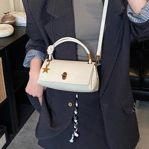 Minimalist beige leather handbag with star charm and gold lock shown in a lifestyle setting