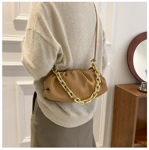 Detailed view of caramel pleated handbag with chunky gold chain strap worn by a model