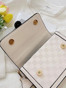 Close-up of cream crossbody bag featuring checkered embossed texture and gold magnetic clasp