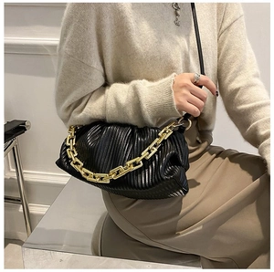 Detail of black pleated cloud bag with chunky gold chain strap on shoulder