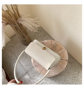 Detail view of cream white rectangular shoulder bag with golden metallic twist lock