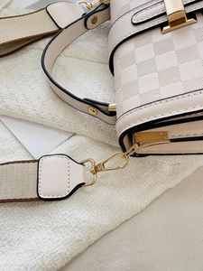 Close-up of cream crossbody bag with checkered embossing and golden metal hardware details