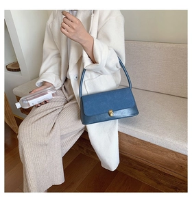 Detail of dark blue baguette shoulder bag featuring a gold square buckle and matte finish