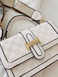 Close-up of golden H-shaped metal buckle on cream crossbody bag with textured pattern