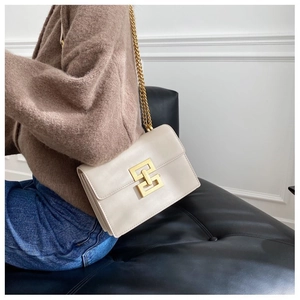 Detail of a beige leather crossbody bag with a chunky gold chain and geometric metal buckle