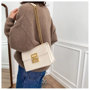 Side view of white crossbody chain bag with gold metal lock on a model in minimalist interior