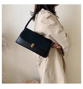 Detail view of a vintage black leather baguette bag with a gold buckle and shoulder strap