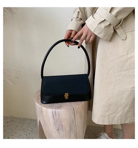 Minimalist black leather handbag with golden metal buckle styled on a wooden stool