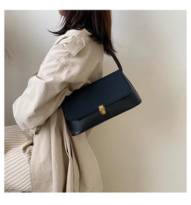 Detail of black underarm bag with gold metal buckle shown on a trench coat model