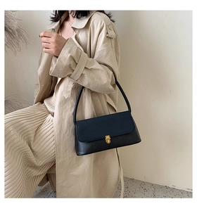 Close-up of black leather handbag with gold metal clasp on a beige trench coat
