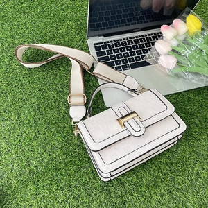 Close-up of white woven pattern crossbody bag with gold metal buckle on green grass