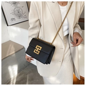 Detail of a black leather crossbody bag with a gold H-shaped buckle and metal chain strap