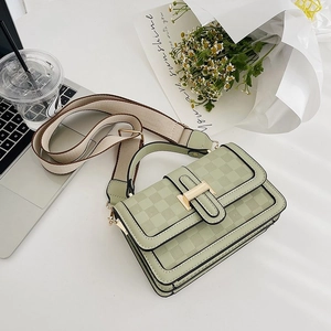 Sage green crossbody bag with checkered texture and wide fabric strap on a desk