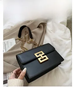 Detail of matte black leather bag with gold geometric lock and chain strap on blazer