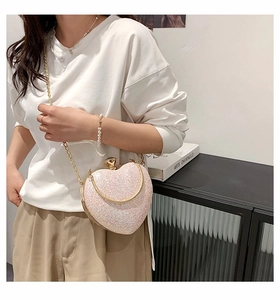Detail of a pink heart-shaped bag with glitter texture and golden metal chain strap