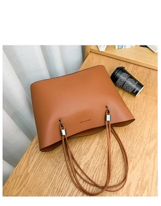 Detail view of caramel faux leather tote bag showing Forever Young logo and metal buckle