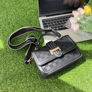 Close-up of black checkered crossbody bag with gold H-lock on green grass with tulips
