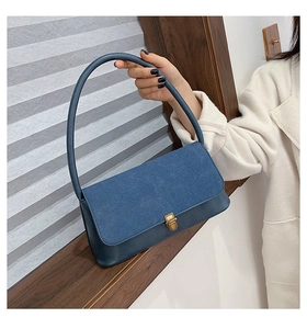 Detail of a vintage denim handbag with leather base and bronze buckle in an indoor setting