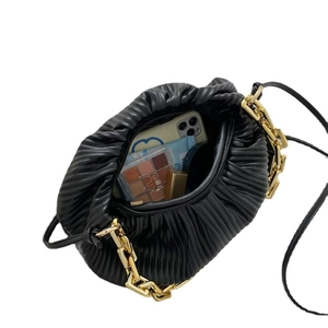 Black ruched clutch bag with chunky gold chain and interior items on white background