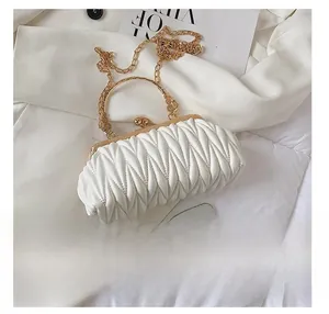 Detailed view of quilted white clutch with gold handle and metal ball clasp beside a phone