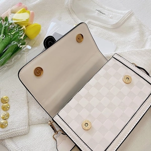 Detail of white quilted crossbody bag with golden magnetic buckles and checkered texture