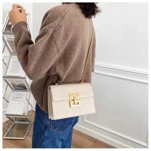 Detail of a beige crossbody bag with gold square metal lock and chain strap on a model
