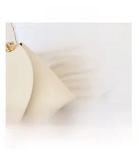 Detail view of white leather handbag featuring gold cylindrical metal clasp and stitching