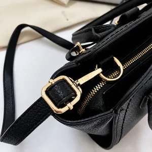 Close-up of golden metal zipper and D-ring on black litchi grain leather handbag