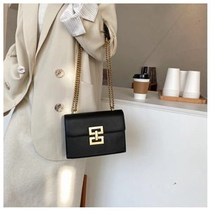 Detailed view of a black leather crossbody bag featuring a gold geometric metal lock