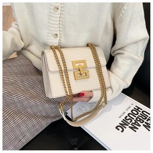 Detail of a beige crossbody bag featuring a large golden metal lock and chain strap