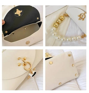 Macro detail of white pearl chain strap, golden hardware, and base studs on handbag