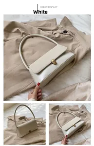 Detail view of a white faux leather baguette bag with a gold clasp on a beige trench coat