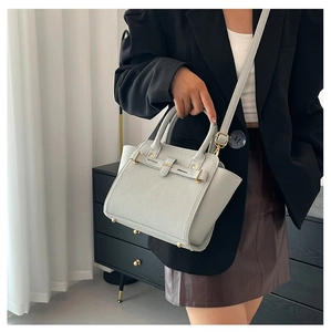 Detail of light gray lychee grain leather handbag with gold rivets and crossbody strap
