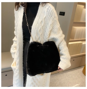 Detail of black faux fur crossbody bag with gold chain strap on white knit cardigan