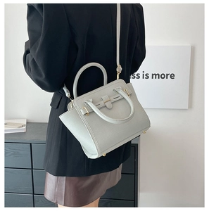 Detailed view of light gray lychee grain leather handbag with gold hardware on a model