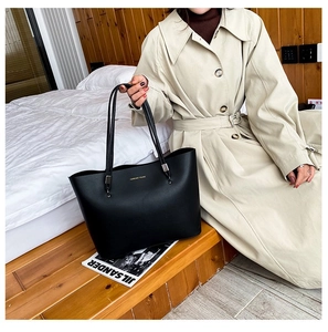 Detail of black matte leather tote bag with gold lettering and long shoulder strap