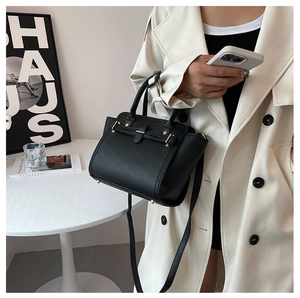 Close-up of black grainy leather handbag with gold buckle and adjustable strap