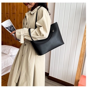 Detail of a large black tote bag on a model wearing a trench coat in a modern setting