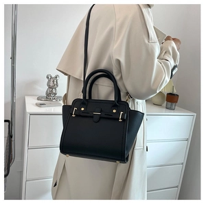 Detail of black textured crossbody bag with gold hardware worn with beige trench coat