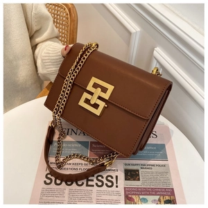Detail of a brown leather crossbody bag with a gold interlocking clasp and chain strap