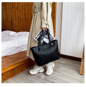 Detail of black leather tote bag featuring gold Forever Young lettering and metal hardware