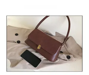Detail view of brown shoulder bag with suede flap and gold buckle next to a phone for scale