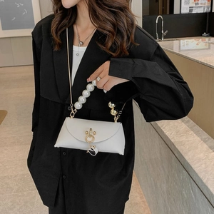 Close-up of white crossbody bag with large pearl handle and gold chain on black shirt