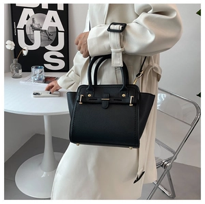 Close-up of black lychee grain leather handbag with gold buckle held by a model