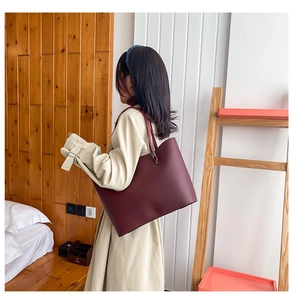 Deep burgundy leather tote bag shown on shoulder of model in beige trench coat