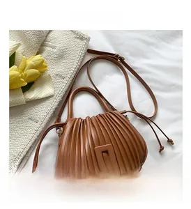 Detail of a brown pleated bucket bag with square buckles on white fabric background