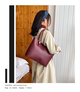 Model wearing a large burgundy tote bag in a stylish interior setting with wooden walls